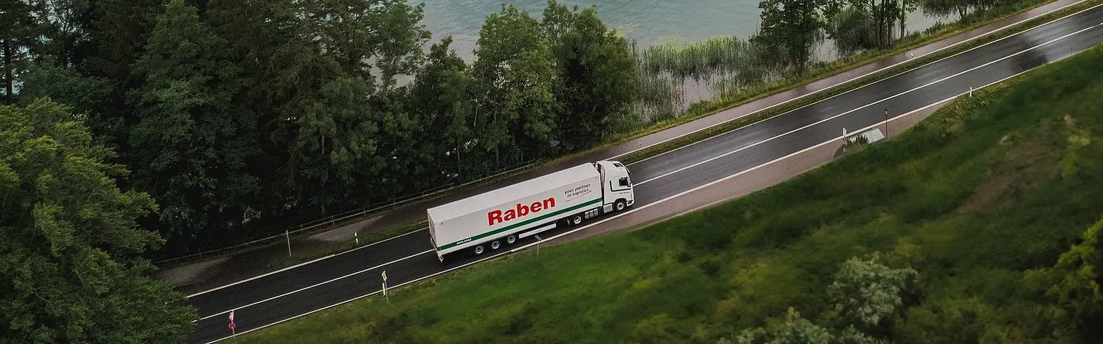 Nákladní vozidlo Raben Group projíždějící krajinou kolem jezera a lesa jako symbol udržitelné logistiky.