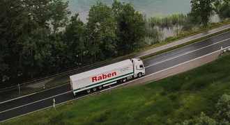 Nákladné vozidlo Raben Group prechádzajúce krajinou pozdĺž jazera a lesa, symbolizujúce udržateľnú prepravu.